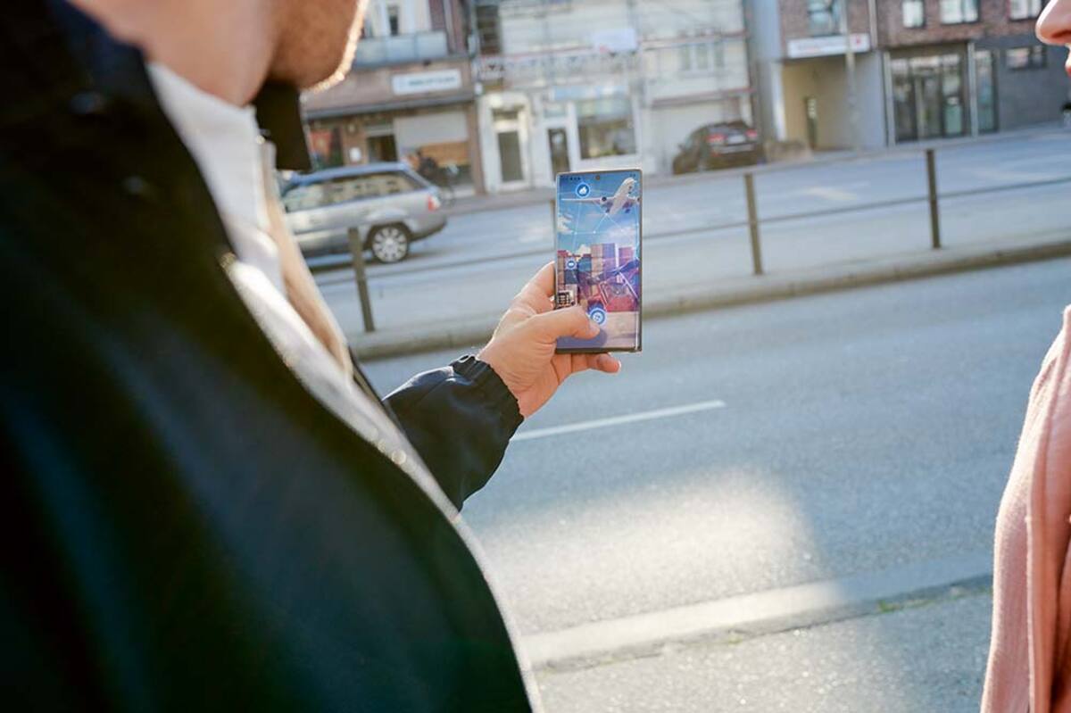 Mężczyzna trzyma w dłoni smartfon. W tle zabudowania miejskie.