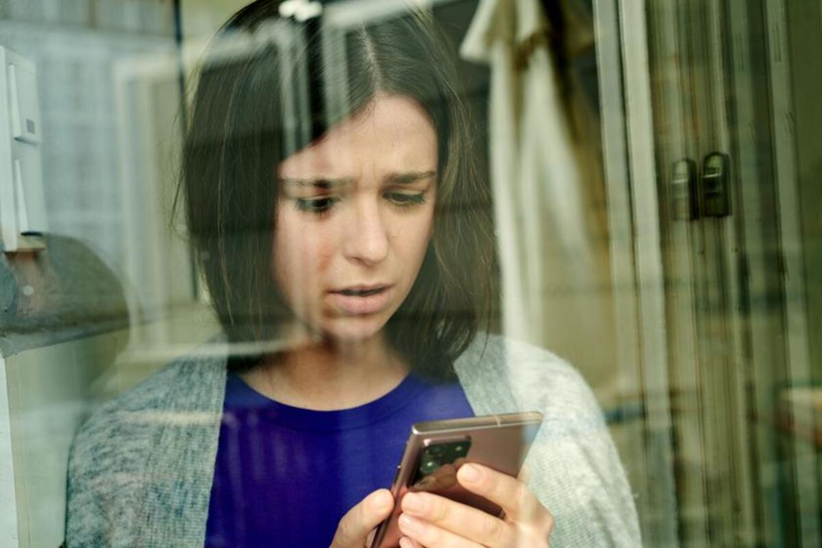 Zmartwiona dziewczyna trzymając w dłoniach smartfon, patrzy na jego ekran