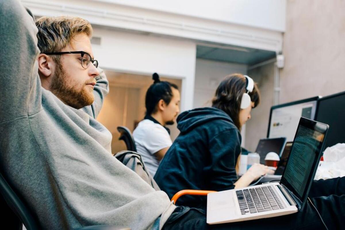 Mężczyzna patrzy na ekran laptopa. W tle dwie osoby pracują na komputerach.