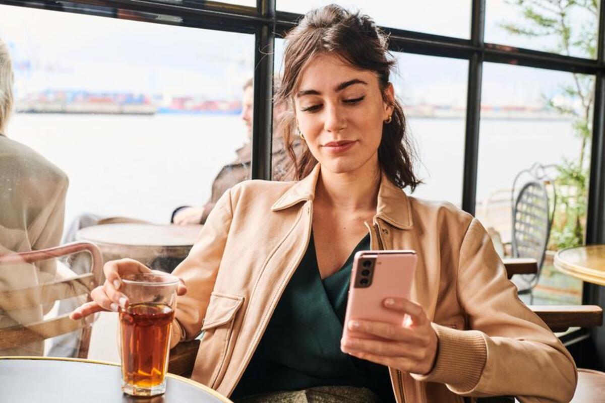 Brunetka siedząca w kawiarni patrzy na telefon.