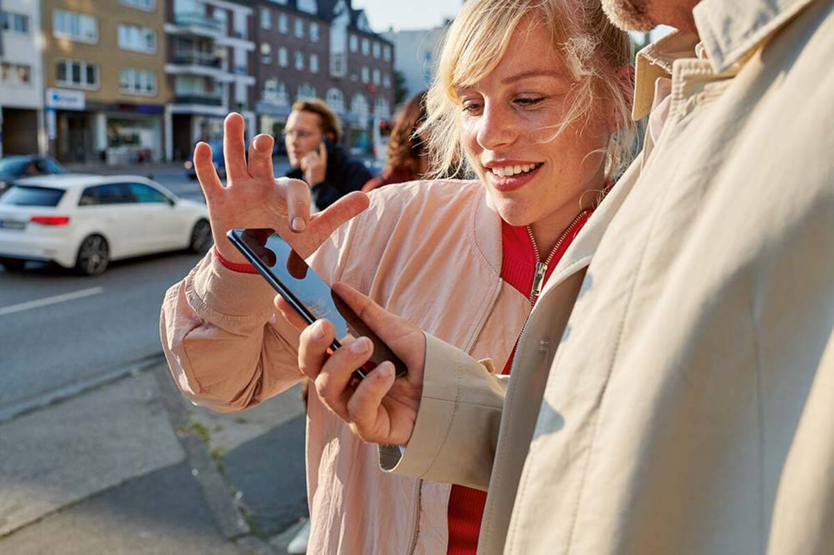 Młoda dziewczyna na ulicy objaśnia mężczyźnie, jak obsługiwać smartfon